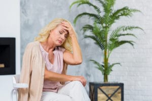 Middle-aged woman seated indoors, holding her forehead in discomfort amid signs of perimenopause.